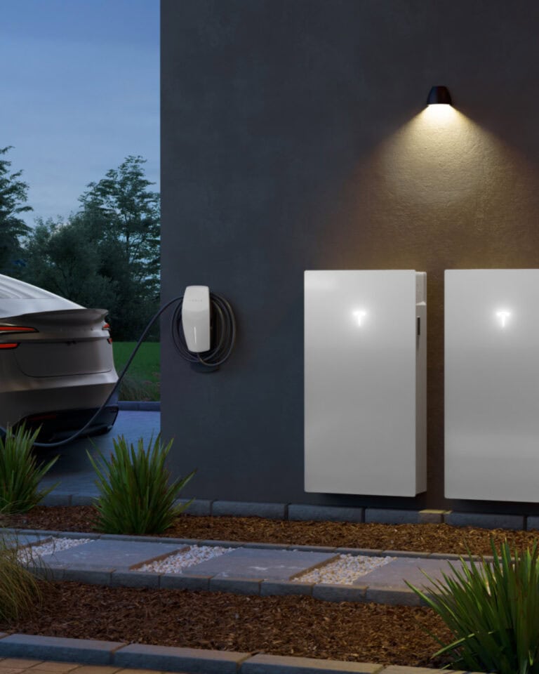 Two Tesla Powerwalls installed outside a hose next to a electric vehicle charger